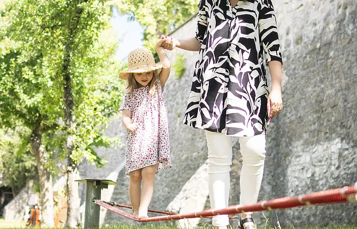 Eine Mama hilft ihrem Kind beim balancieren auf der Slackline im Stadtgraben.