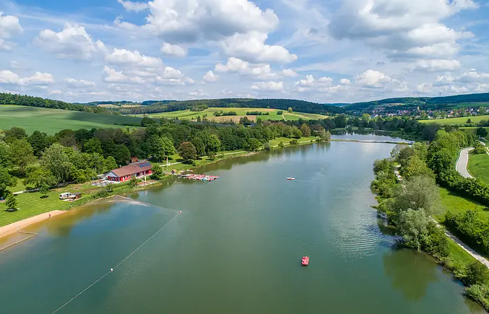 Hahnenkammsee von Süden nach Norden mit Strandanlage links, Seeterasse und Badestrand