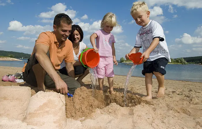 Eine vierköpfige Familie spielt am Strand des Brombachsees in Ramsberg. Die zwei Kinder erfreuen sich am sandeln und genießen die Zeit.