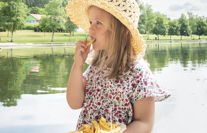 Mädchen isst Pommes auf der Seeterrasse am Waldsee.