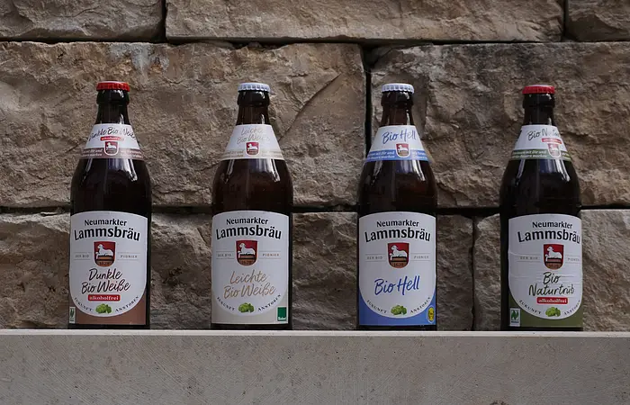 Vier Flaschen Neumarkter Lammsbräu Bier stehen vor einer Steinwand.