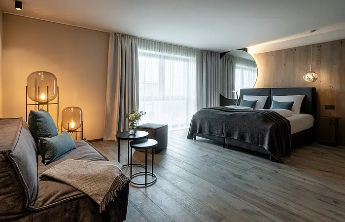 Modernes Schlafzimmer mit Doppelbett, Sofa, zwei runden Tischen, großen Fenstern und Holzfußboden.