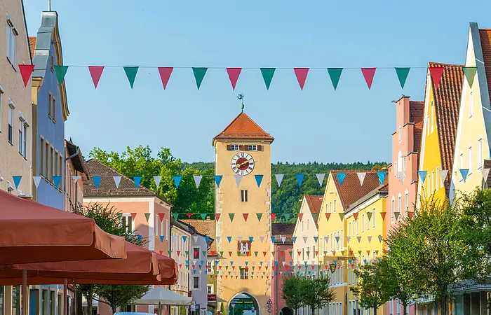 Der Blick geht in Richtung eines Torturms. Links und rechts sind die Giebel historischer Häuser zu sehen, zwischen denen bunte Wimpel gespannt sind.