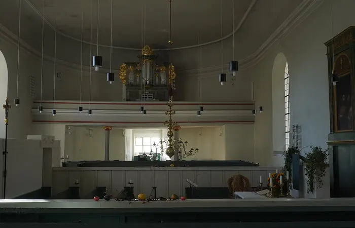 Innenraum einer Kirche mit Orgel, Kronleuchter, Kerzen und Fenstern an den Seitenwänden.