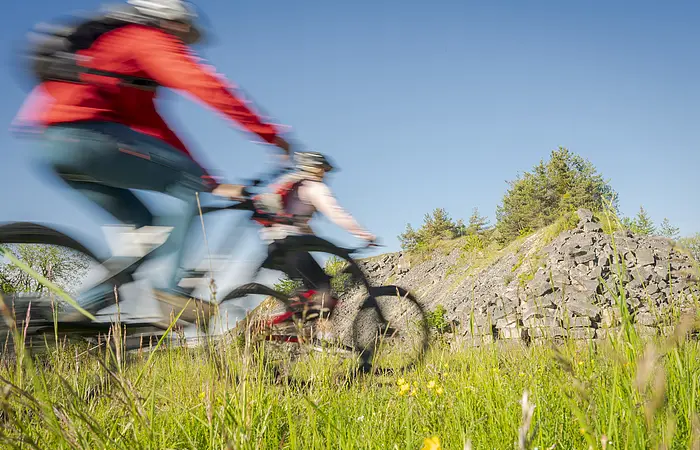 Zwei Fahrradfahrer die Fahrrad fahren und im Hintergrund ist ein kleiner Berg zu sehen