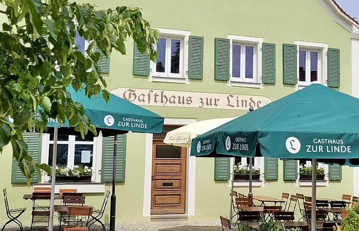 Der Gasthof ist von außen grün gestrichen und hat etwas dunklere Fensterläden ebenfalls in grün. Der Biergarten ist aufgebaut und lädt bei Sonnenschein zum Verweilen ein.