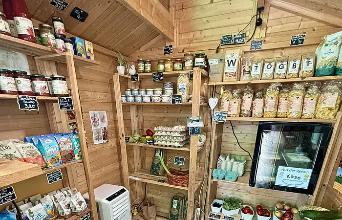 Kleiner Holzladen mit Regalen voller Lebensmittel, Eiern, Obst, Gemüse und Getränken.