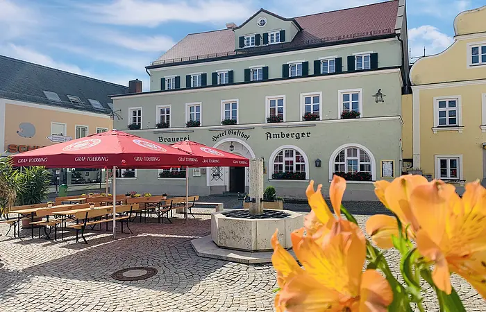 Die Vorderansicht des Braugasthofes mit Eingang und davor der Biergarten mit rotem Sonnenschirm.
