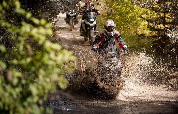 Mottorradfahrer fahren mit ihren Maschinen durch Matschpützen. Das Wasser spritzt.
