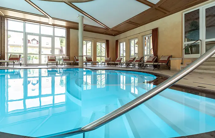 Der hellblaue Swimmingpool ist im Vordergrund. Links sieht man die Fensterfront mit Blick in den Garten. Rechts sieht man die Liegen, die um den Pool aufgereiht sind.