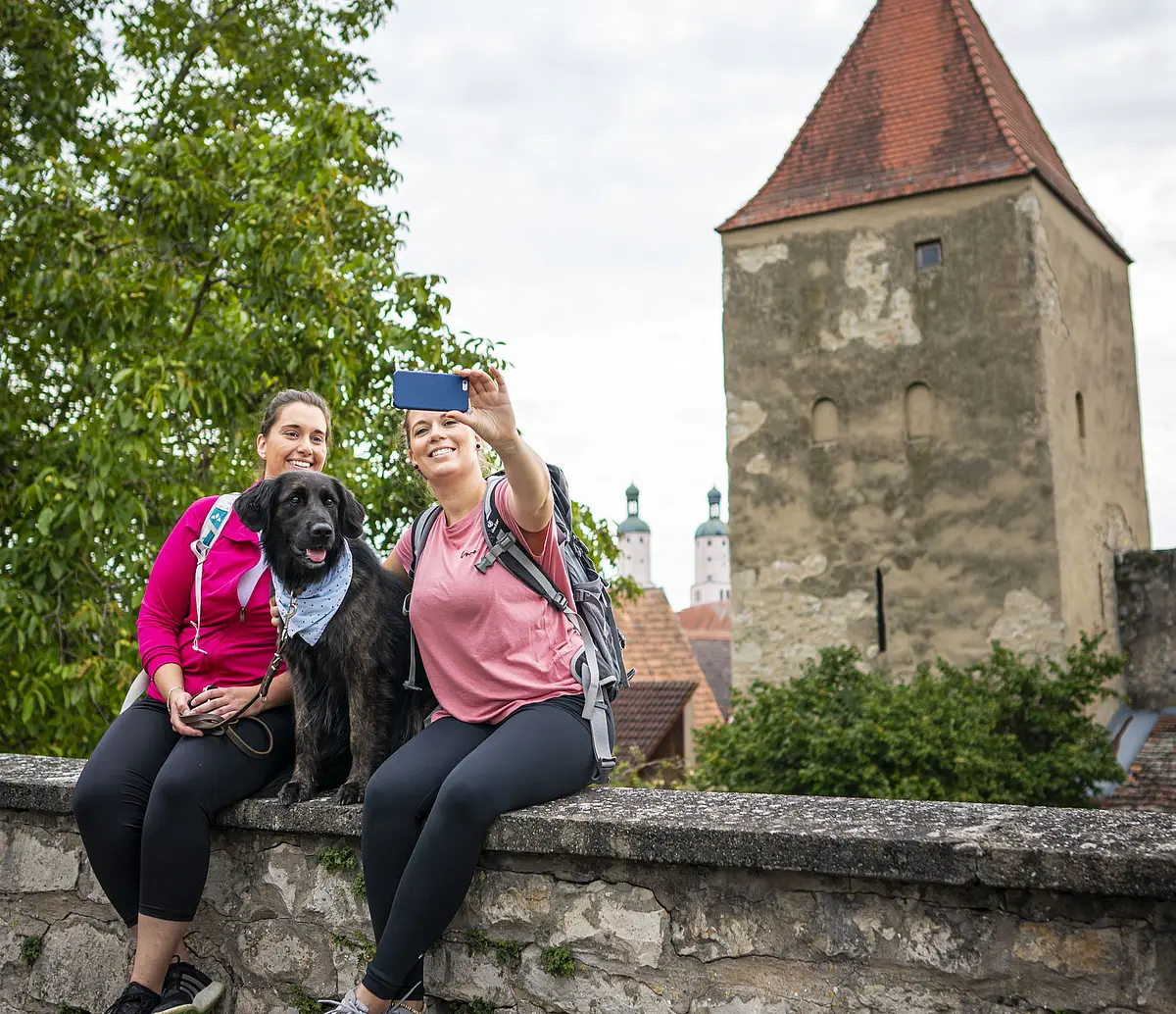 Baronturm Zwei Freundinnen sitzen mit ihrem Hund auf der Stadtmauer und machen ein Selfie mit dem Baronturm.