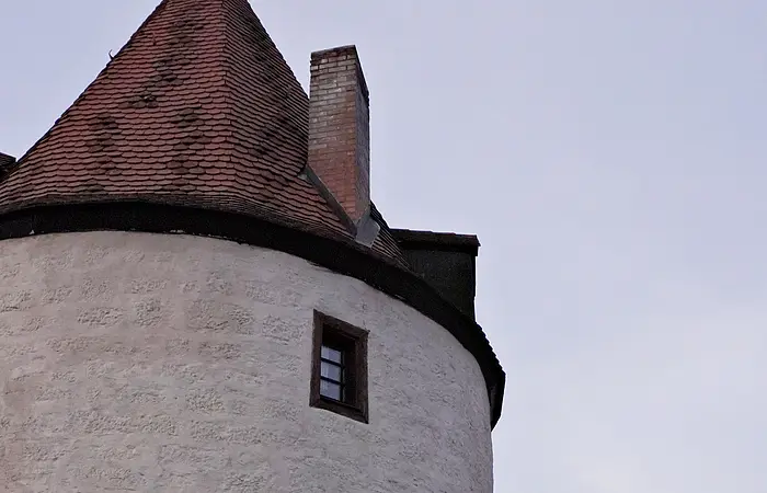Runder weißer Turm mit roten Dachziegeln, zwei kleinen Fenstern und Laterne an der Wand bei Dämmerung.