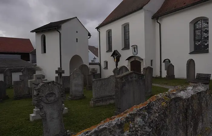 Friedhof mit alten Grabsteinen vor weißen Kirchengebäuden unter bewölktem Himmel.