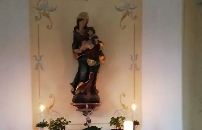 Altar mit Statue der Marienstatue, Kerzen auf dem Altar, sowie Blumen und Pflanzen in einem kleinen Raum einer Kapelle.