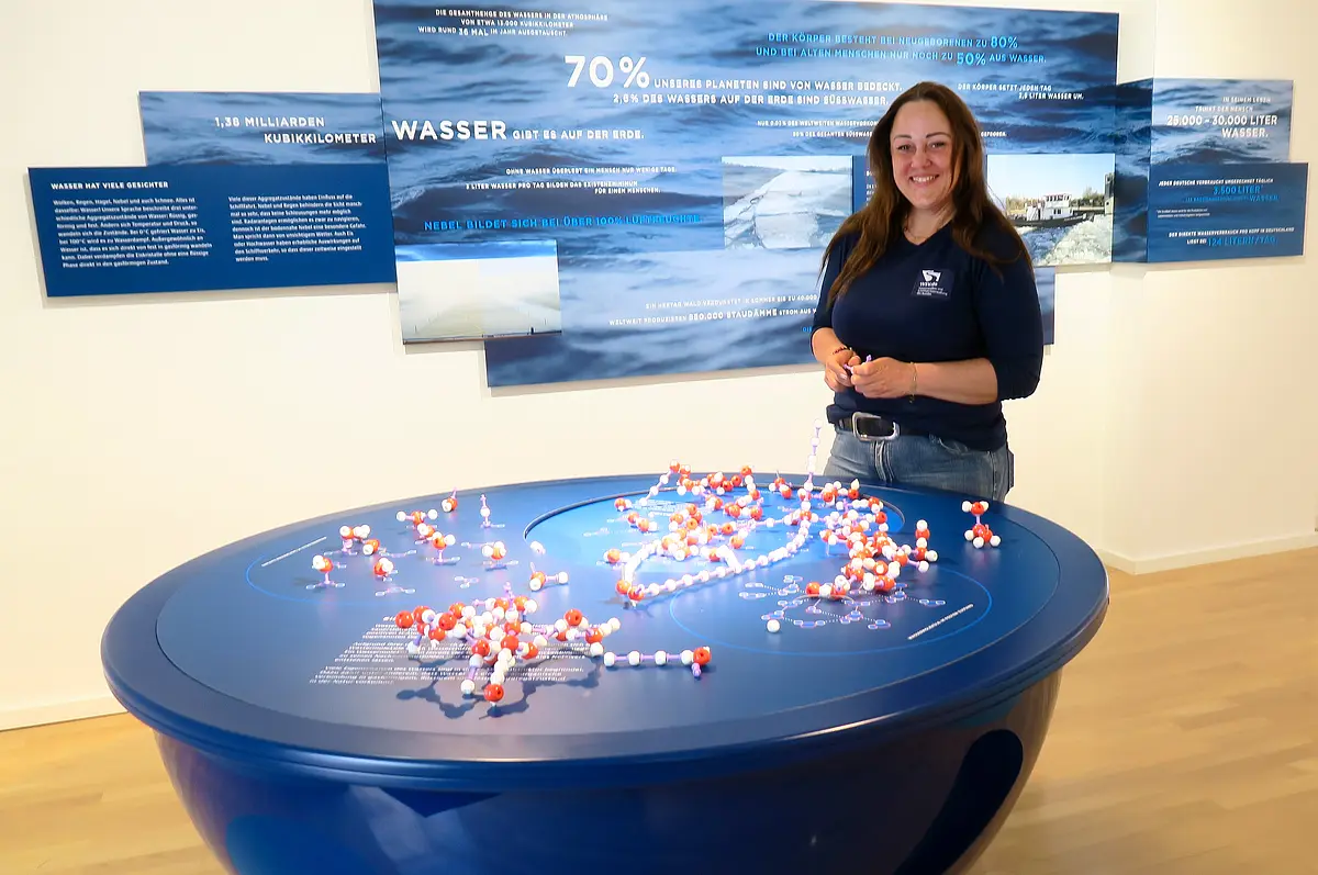 Frau steht vor Ausstellungstisch mit Molekülmodellen, im Hintergrund Infotafeln zum Thema Wasser.