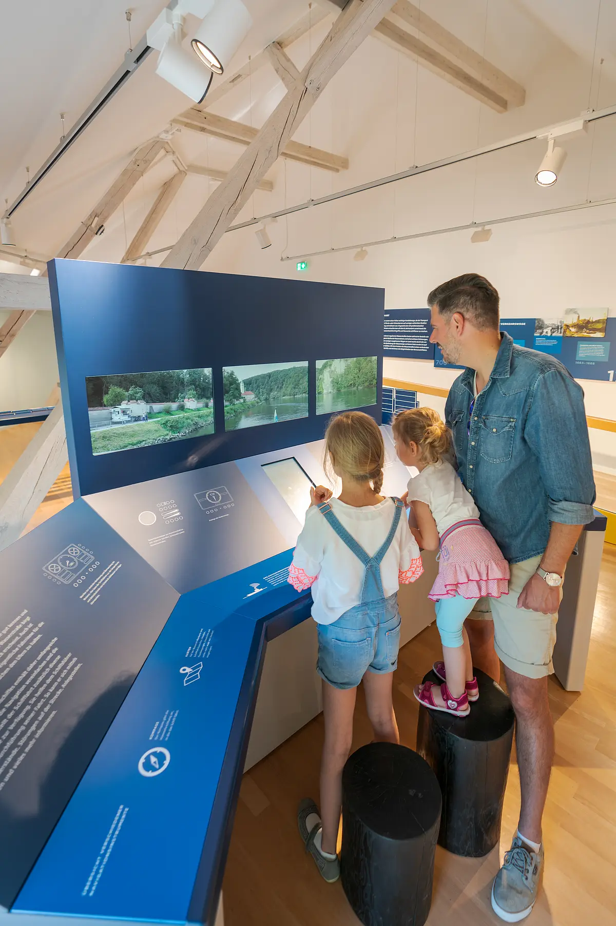 Mann und zwei Kinder vor Bildschirmen an interaktiver Station