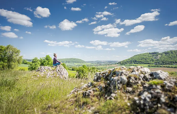 Frau sitzt auf einem Stein in Yogapose im Vordergrund ein Felsen