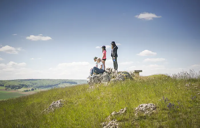Familie mit Hund sitzen auf dem Bubenheimer Berg auf einem Felsen. Kinder stehen hinter den Eltern