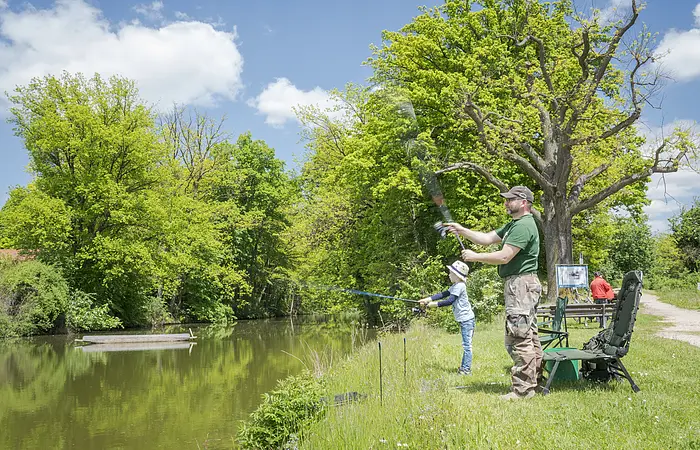 Vater und Sohn angeln am Karlsgraben. Vater steht und holt den Fisch aus dem Gewässer.