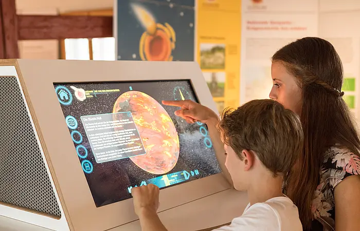 Zwei Kinder schauen sich die Infomationen auf dem Infoterminal im Geopark Infozentrum in Nördlingen an