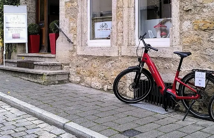 Ein rotes Fahrrad steht vor der Eingangstür eines Gebäudes/Laden der Firma rent a bike in Rothenburg o.d. Tauber