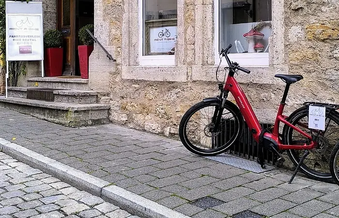 Ein rotes Fahrrad steht vor der Eingangstür eines Gebäudes/Laden der Firma rent a bike in Rothenburg o.d. Tauber