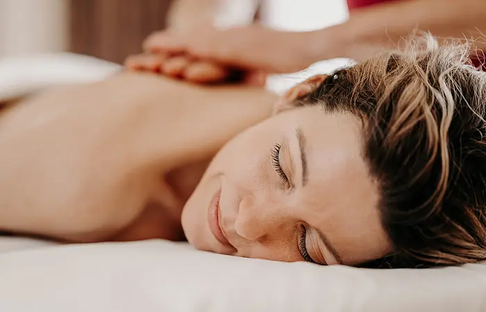 Eine Frau liegt auf dem Rücken auf einer Massageliege. Ihr Rücken wird von Händen massiert.