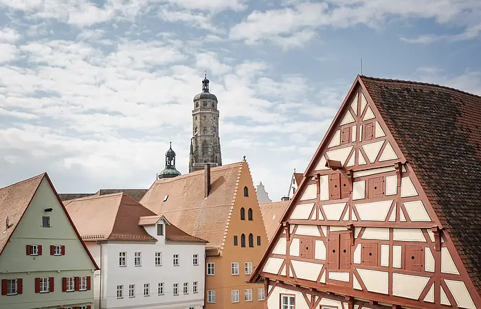 Fachwerkhäuser mit roten Dächern, im Hintergrund ein Kirchturm unter blauem Himmel.