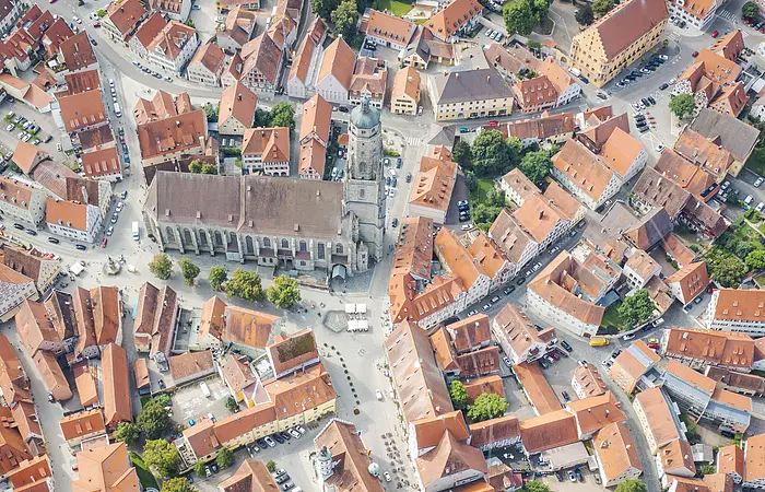 Luftaufnahme einer Stadt mit einer großen Kirche im Zentrum, umgeben von Gebäuden mit roten Dächern und Straßen.