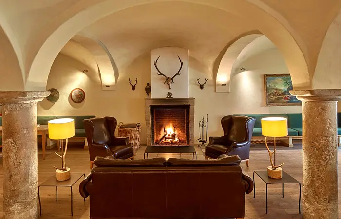Wohnzimmer mit gewölbter Decke, Kamin, Ledersesseln, Sofa, zwei Lampen und Hirschgeweihen an der Wand.