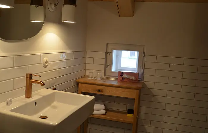 Eine Badezimmer der Gasthof Krone Kinding mit Waschbecken im Vordergrund und im Hintergrund ein Beistelltisch mit Spiegel
