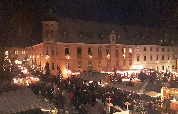 Kloster Plankstetten bei Nacht Vor dem Gebäude sind Stände Adventsstände aufgebaut, belebt mit Menschen. Alles ist weihnachtlich beleuchtet.