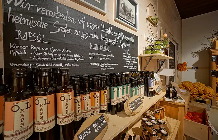 Flaschen mit Rapsöl vor Tafel mit handgeschriebenen Informationen zu Ölen in einem Holzladen.