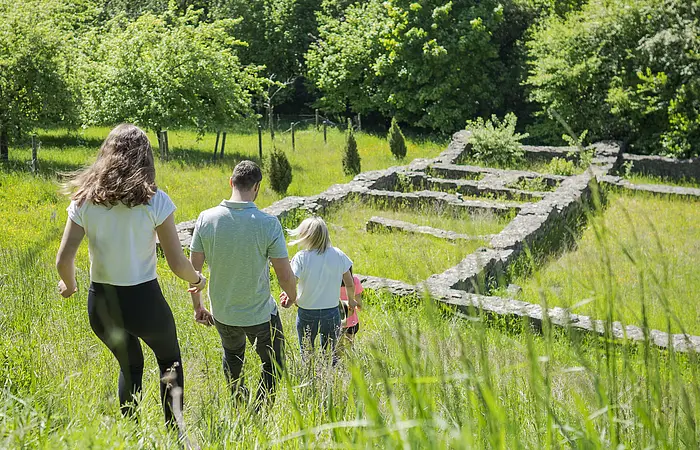 Familie läuft durch die Wiese auf die Villa Rustica zu