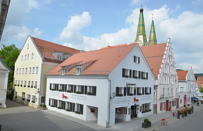 Das Hotel an der Ecke ist weichgestrichen mit grünen Fensterläden. Im Hintergrund sind grüne Kirchtürme zu erkennen.