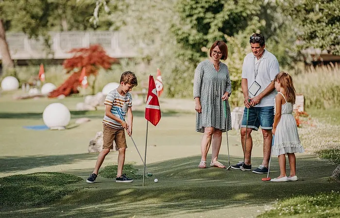 Eine Familie steht vor einem Loch und schaut dem Junior beim letzten Schlag zu.