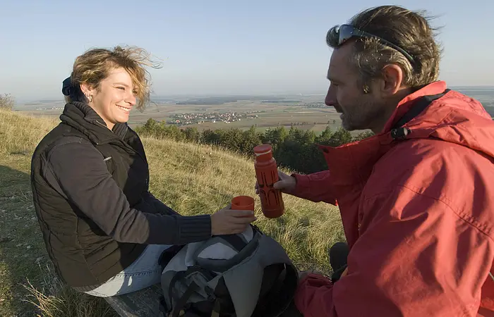 Frau und Mann stoppen und trinken im Herbst einen heißen Tee auf einer gelen Wiese.