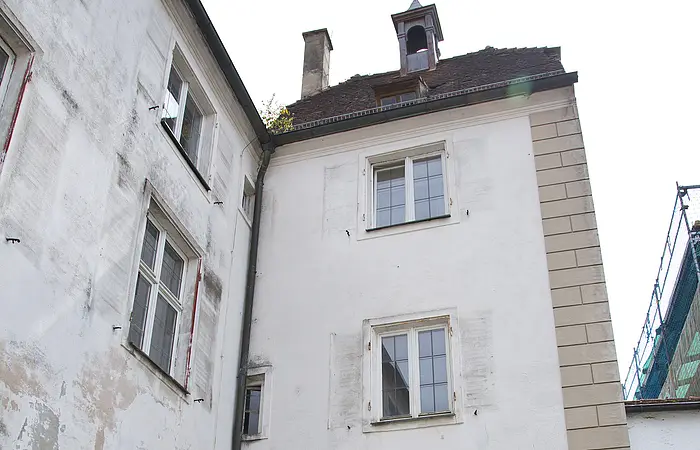 Historisches Stadttor mit Durchfahrt entlang einer Kopfsteinpflasterstraße. Das Tor und das Gebäude links daneben mit einer weiß verputzten Fassade und Verkehrsschildern rechts am Torbogen. Vor dem Tor ein kleines bepflanztes Beet.