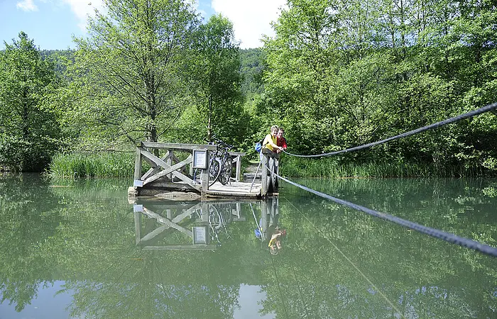 Mit eigener Kraft ziehen Radfahrer auf dem Holzfloß über den Alten Kanal bei Dietfurt.