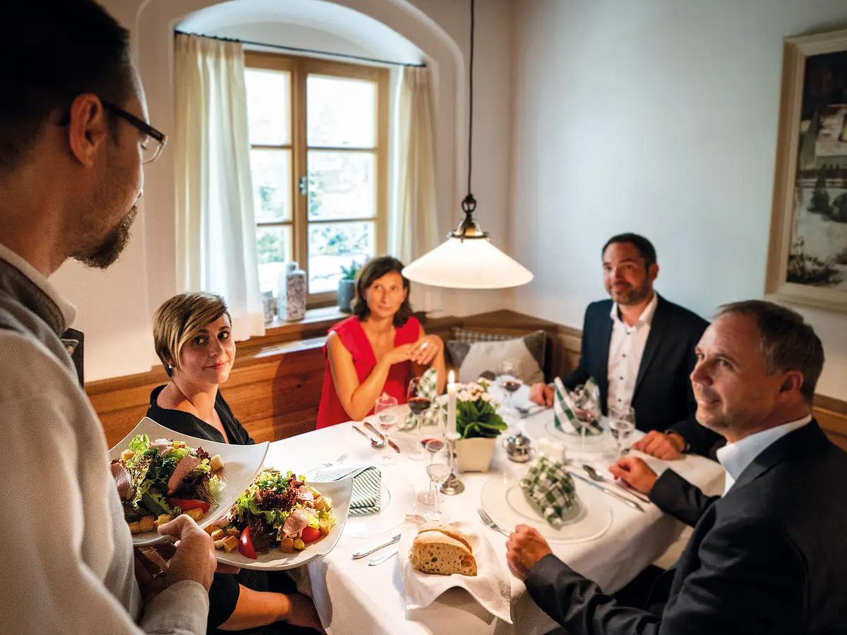 Im Gasthof Millipp in Beilngries Eine Gruppe von vier Personen sitzt an einem gedeckten Tisch in einem Restaurant, während ein Kellner Essen serviert.