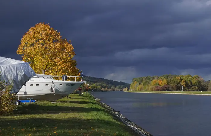 Boot mit dem Namen Liberty am Ufer eines Flusses, herbstliche Bäume und dunkler Himmel im Hintergrund.