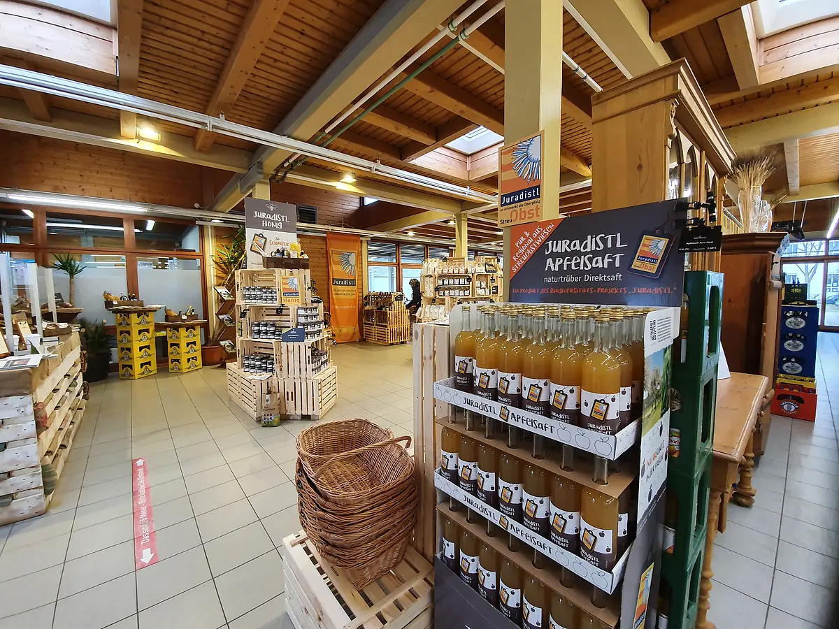 Verkaufsraum mit Holzbalkendecke und Regalen mit regionalen Produkten wie Apfelsaft und Honig.