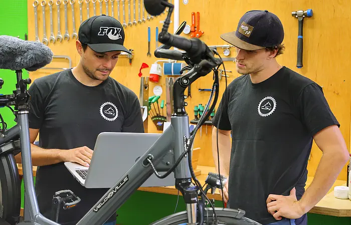 Auf dem Bild sieht man Schmid Maximilian u. Quirin, die beiden schauen in den PC und reparieren ein E-Bike.