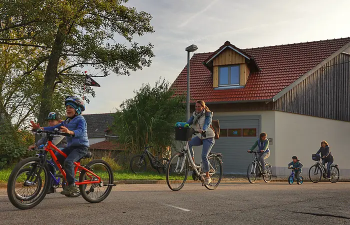 Mehrere Kinder und Erwachsene fahren mit dem Fahrrad bei der Werkstatt vorbei.