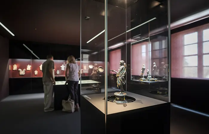 Im Vordergrund ist eine Glasvitrine mit einem römischen Exponat. Im Hintergrund schauen sich eine Frau und ein Mann die Exponate an.