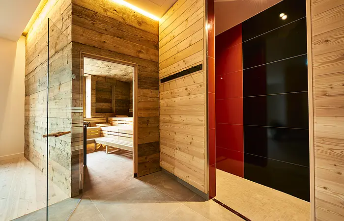 Die Glastür der Sauna aus Holz steht offen und wir können einen Blick auf die leeren Bänke darin werfen.