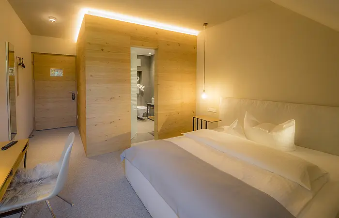 Hotelzimmer mit Doppelbett, Schreibtisch, Stuhl, Holzwand und offenem Bad mit Toilette und Handtüchern