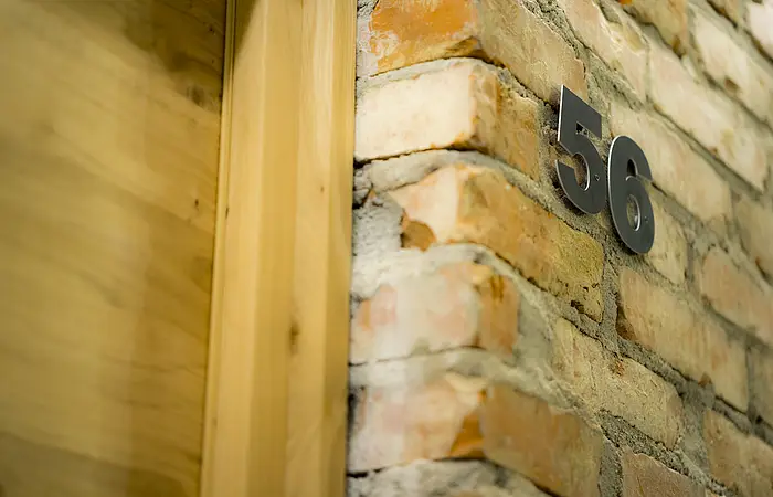 Hausnummer 56 an einer Backsteinwand neben einem Holztürrahmen.
