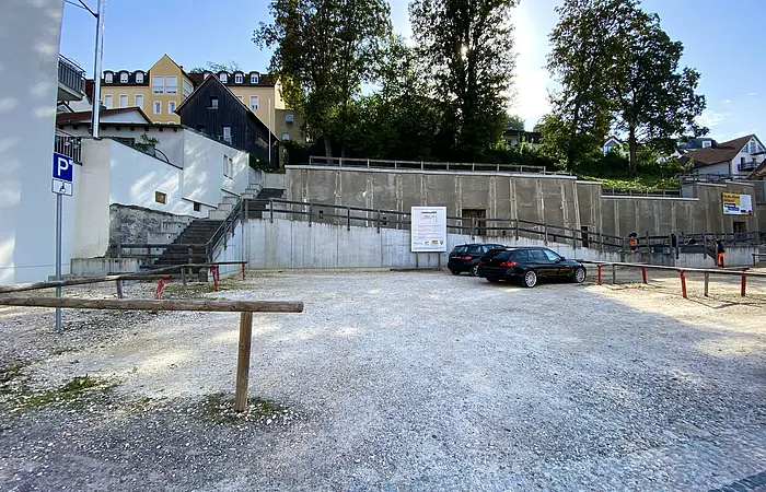 Parkplatz mit zwei schwarzen Autos, Treppen und Bäumen im Hintergrund bei sonnigem Himmel
