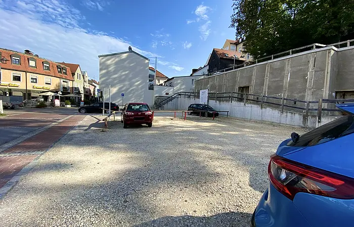 Parkplatz mit drei geparkten Autos vor Gebäuden und blauem Himmel bei Tageslicht